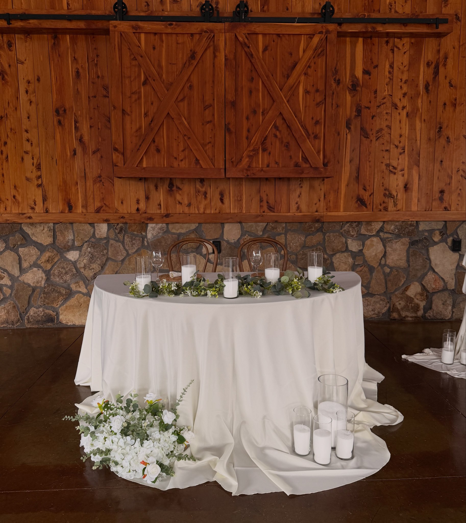 Mesa romántica con telas blancas, flores y velas frente a puertas de madera